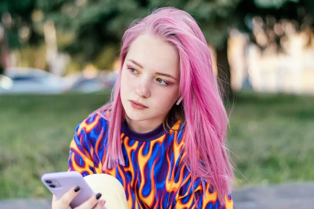 Gen Z Teenager with pink hair holding a phone